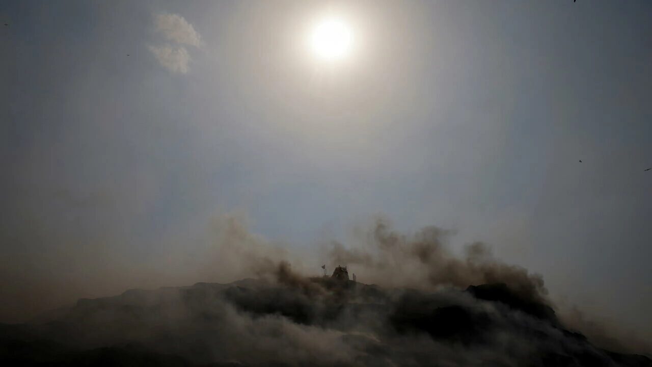 An excavator tries to contain the fire as smoke billows from burning garbage on a hot summer day, at the Bhalswa landfill site in New Delhi, India, April 29, 2022.