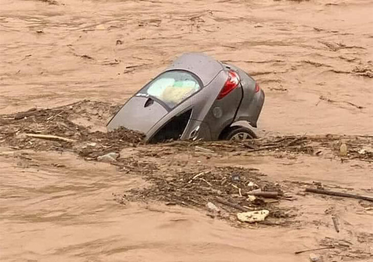 A car is half swallowed by floodwaters.