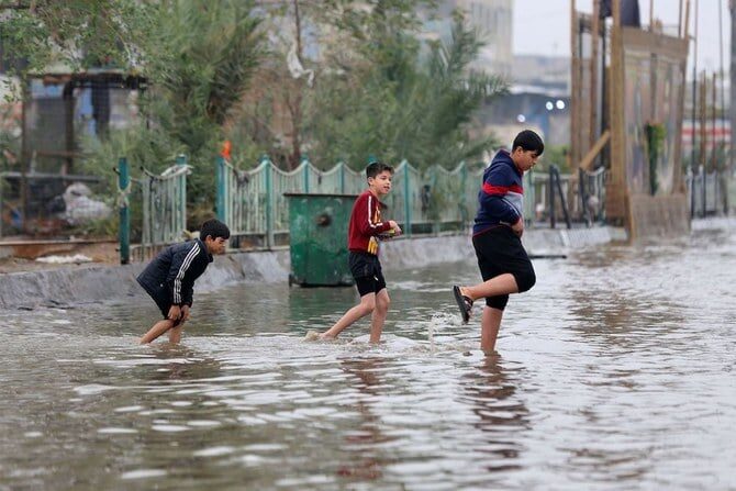 Iraqi children cross a flooded street in the Iraqi