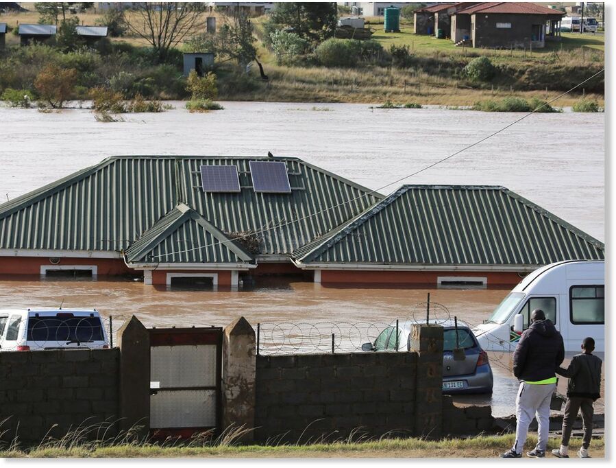 A man with a child look at a home submerged in floodwater in Mthatha