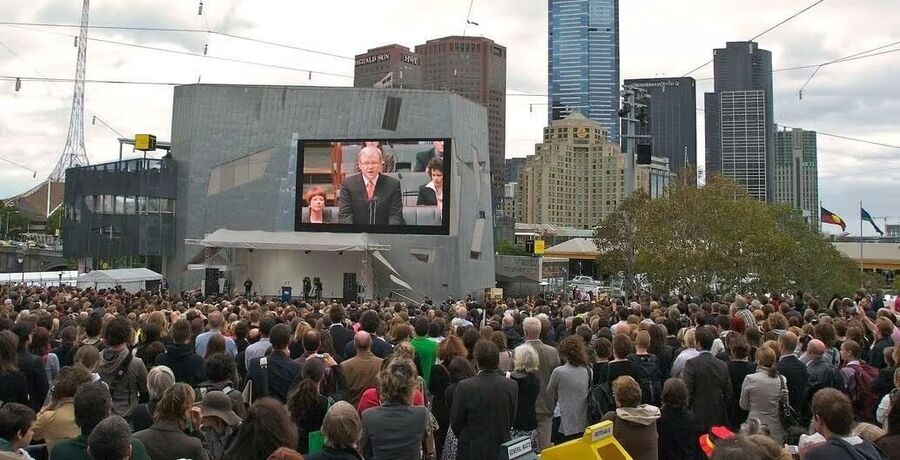 Klikni za povećanje People gathered listening to a politician on a screen